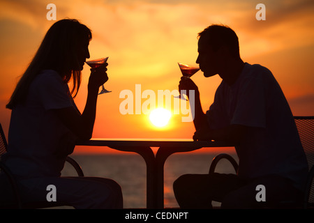 Frau und des Mannes Silhouetten auf Sonnenuntergang trinken aus Gläsern Stockfoto