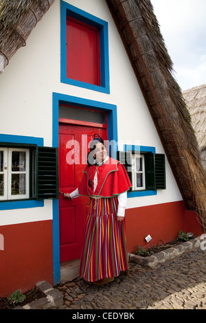 Traditionelles, dreieckiges portugiesisches Haus mit einem Strohdach von Palheiro. Frau in traditioneller Tracht aus mehrfarbigen Stoffen Santana, Madeira Stockfoto