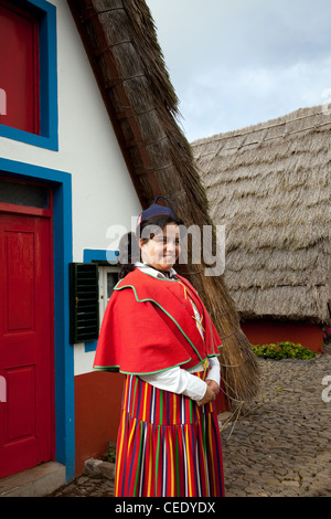 Traditionelles, dreieckiges portugiesisches Haus mit einem Strohdach von Palheiro. Frau in traditioneller Tracht aus mehrfarbigen Stoffen Santana, Madeira Stockfoto