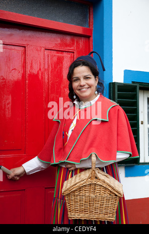 Traditionelles, dreieckiges portugiesisches Haus mit einem Strohdach von Palheiro. Frau in traditioneller Tracht aus mehrfarbigen Stoffen Santana, Madeira Stockfoto