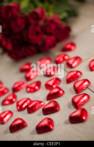 Schokoladenherz geformte Süßigkeiten eingehüllt in roten Folie und rote Rosen Stockfoto