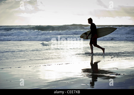 Silhouette eines Surfers zu Fuß mit seinem Surfbrett entlang des Strandes mit stürmischen Wolken im Hintergrund, Tarifa, Andalusien, Spanien Stockfoto