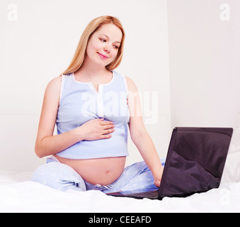 Schwangere Frau mit Laptop im Bett Stockfoto