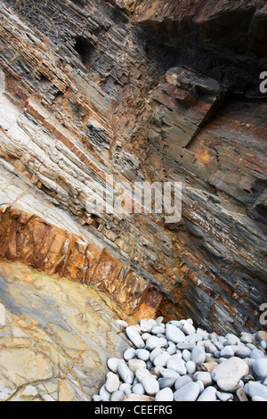 Nahaufnahme von bunten Gesteinsschichten am Sandymouth Strand. Es gibt einen Haufen von grauen Kieseln am Fuße der Felswand. Stockfoto