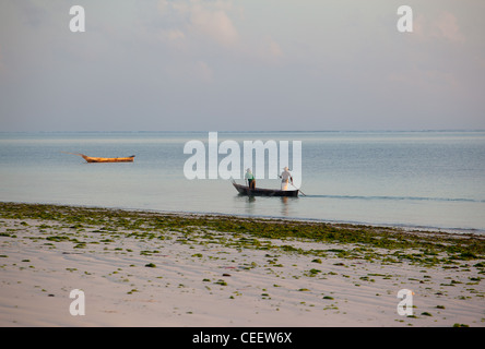 Sansibar Herren Stechkahn fahren einer hölzernen Dhau im Meer vor der Coral reef er Korallenriff, wo die Wellen brechen in der Ferne in Bwejuu, Sansibar, Tansania Stockfoto