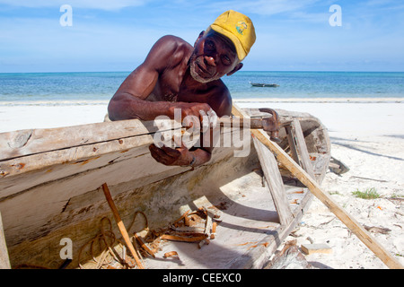 Zanzibari Greis Reparatur einer hölzernen Dhau am Strand von Bwejuu, Sansibar, Tansania Stockfoto