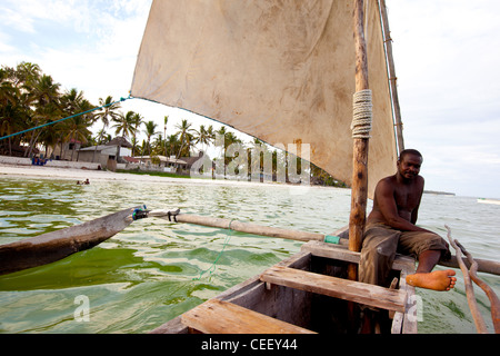 Zanzibari Mann sitzt in der Bögen von einer Dhau Segeln, im Meer vor dem Korallenriff in Bwejuu, Sansibar, Tansania Stockfoto