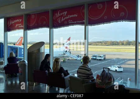 dh Abflughalle SCOTTISH AIRPORT EDINBURGH SCHOTTLAND Passagiere betrachten die Landebahn eines Flugzeugs und sehen das Innere des Personenterminals Stockfoto