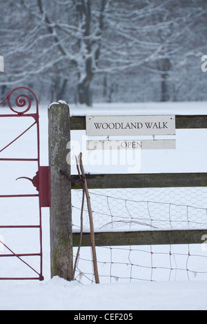 Eine rote Metalltor in einer verschneiten Wiese im Winter, mit einem Schild auf einem Holzzaun besagt Woodland Walk Open Stockfoto