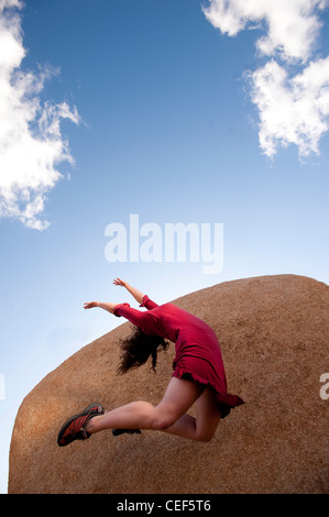 Tänzerin in einem roten Kleid zu einem abstrakten Himmel und Steinlandschaft aufspringend. Stockfoto