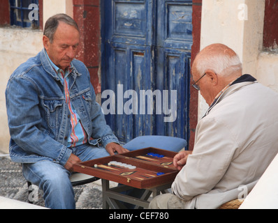 Zwei sitzende griechische Männer spielen Backgammon, verblasste blaue Tür hinter, Santorin, Kykladen, Griechenland Stockfoto