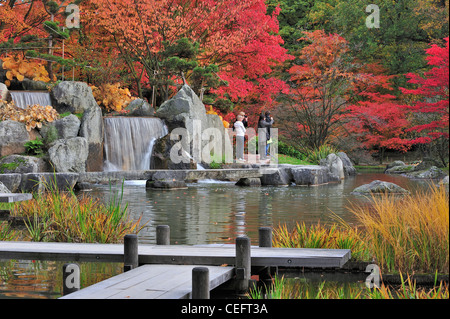 Touristen zu Fuß entlang Teich mit Wasserfall und Ahorn Bäume in bunten Herbstfarben im japanischen Garten, Hasselt, Belgien Stockfoto