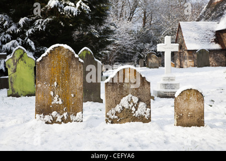 St.-Nikolaus Kirche, Church Hill, Pyrford, Surrey, England mit Grab Grabsteine und Kreuz im Friedhof im Schnee Stockfoto