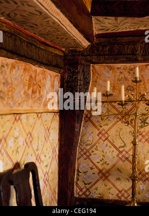 Mittelalterlich anmutenden Mustern bemalt an Wänden des Landes Esszimmer mit hohen Messing Kandelaber und rustikale Holzbalken Stockfoto