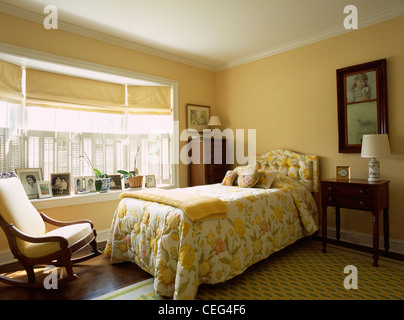 Schaukelstuhl in gelben Reihenhaus Schlafzimmer mit gelben Vorhänge an oben Einzelbett mit gelben Blumen quilt Stockfoto