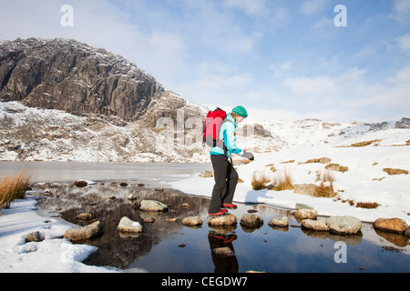 Frau Hill Wanderer durch eine gefrorene scheut Tarn in die saisonabhängige, Lake District, Großbritannien Stockfoto