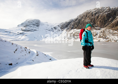 Frau Hill Wanderer durch eine gefrorene scheut Tarn in die saisonabhängige, Lake District, Großbritannien Stockfoto