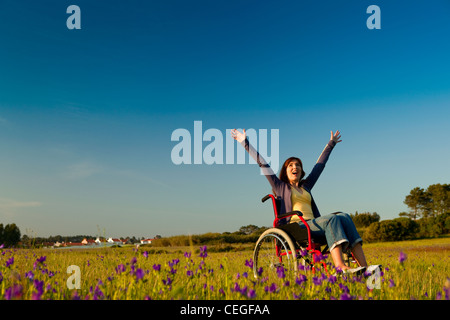 Glückliche behinderte Frau auf einen Rollstuhl über eine grüne Wiese Stockfoto