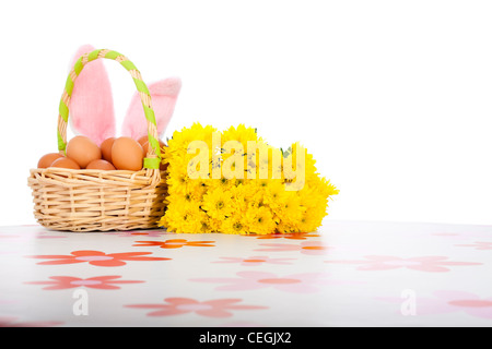 Osterkorb mit Eiern, gelben Blüten und rosa Hasenohren, isoliert auf weißem Hintergrund. Stockfoto