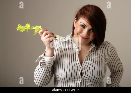 Übergewichtige Frau in einer engen passend Hemd Stand hält einen Stock von Sellerie. Stockfoto