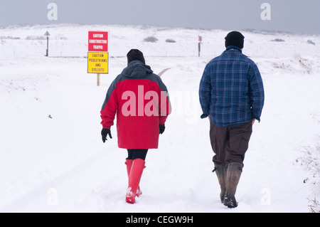 Leute Mann Frau paar Person Rückansicht zu Fuß durch den Schnee tragen Wellington Boots Wintermäntel und Hüte UK Stockfoto