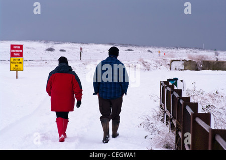 Rückseitige Ansicht von hinten von Mann und Frau Menschen paar zu Fuß durch den Schnee tragen Mäntel Mützen und Wellington Boots UK Stockfoto