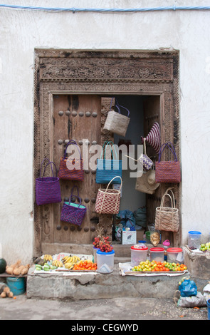 Bunte Taschen und Obst zu verkaufen, hängt an einer herkömmlichen Tür in Stone Town, Sansibar, Tansania Stockfoto