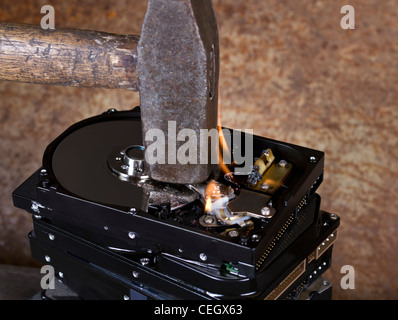 symbolische Daten Zerstörung Thema zeigt die Details eines Hammers auf ein Stapel brennen Festplatten vor rostigen zurück Stockfoto