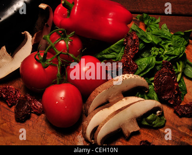 Portabella Pilze, Reben gereifte Tomaten, frischem Basilikum, Auberginen und Sonne getrockneten Tomaten auf ein Schneidebrett. Stockfoto