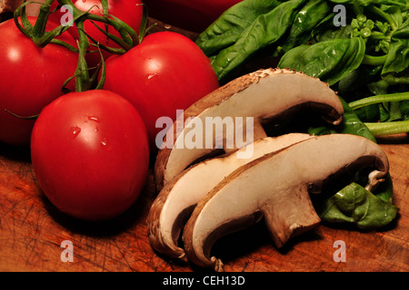 Portabella Pilze, Reben gereifte Tomaten und frischem Basilikum auf ein Schneidebrett. Stockfoto