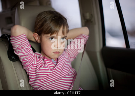 Sechs Jahre altes Mädchen sitzen in einem Auto mit Armen hinter dem Kopf, schmollend. Ernst, Heck, Enttäuschung. Stockfoto