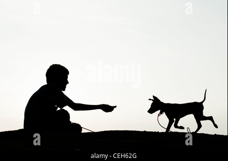 Silhouette des jungen sitzen und spielen mit seinen Welpen. Indien Stockfoto