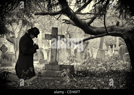 Mann ist auf die Knie unter einem Baum auf dem Friedhof beten. Stockfoto