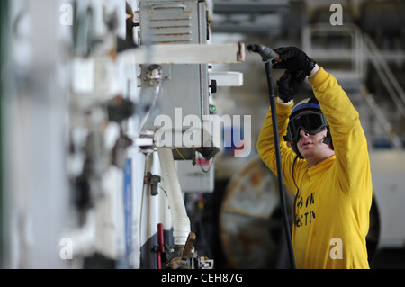 Aviation Boatswain's Mate (Handling) 3rd Class Ryan A. Jones reinigt mit einem Niederdruck-Luftschlauch in der Hangarbucht des Flugzeugträgers USS George H.W. Buchse. George H.W. Bush ist im Atlantischen Ozean und führt die Qualifikationen der Spediteur durch. Stockfoto