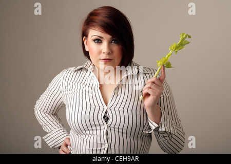 Übergewichtige Frau in einer engen passend Hemd Stand hält einen Stock von Sellerie. Stockfoto