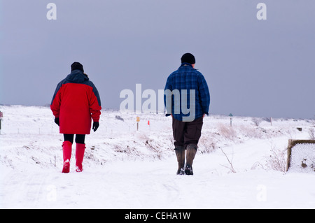 Leute Mann Frau paar Person Rückansicht zu Fuß durch den Schnee tragen Wellington Boots Wintermäntel und Hüte UK Stockfoto