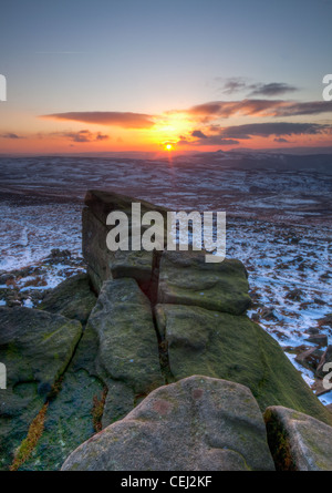 Sonnenuntergang über eine verschneite Landschaft.  Einem Felsvorsprung erstreckt sich von den Zuschauern Füßen gegen die untergehende Sonne knapp über dem Horizont. Stockfoto