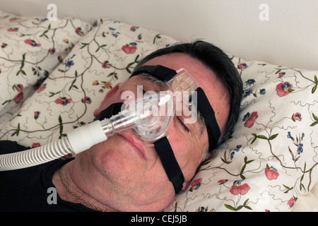 Mann mit einer CPAP-Maske und Maschine verwendet für die Behandlung von Schlafapnoe. Stockfoto