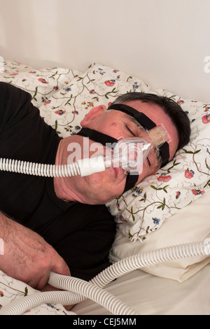 Mann mit einer CPAP-Maske und Maschine verwendet für die Behandlung von Schlafapnoe. Stockfoto