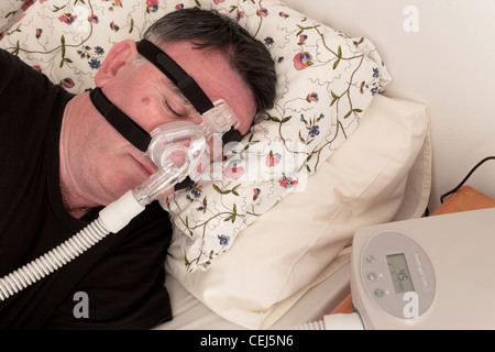 Mann mit einer CPAP-Maske und Maschine verwendet für die Behandlung von Schlafapnoe. Stockfoto