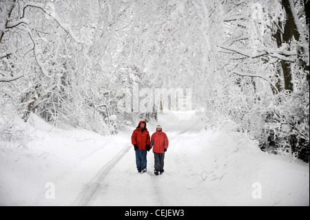 Ein paar in passenden roten Wintermäntel zu Fuß in einer Cotswold-Gasse in Schneeverhältnissen UK Stockfoto