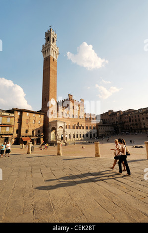 Touristen auf der Piazza del Campo, dem zentralen Platz der Stadt Siena, Toskana, Italien. Torre del Mangia Turm erhebt sich hinter Stockfoto