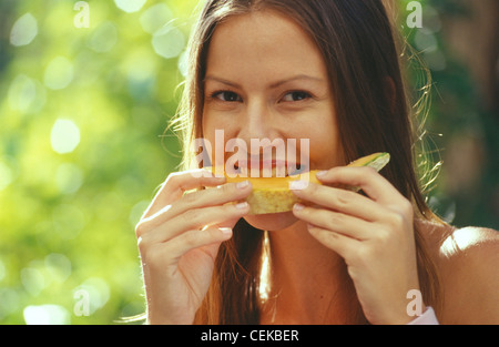 Brünette Frauen gerade Zentrum Abschied Haar, orange Honigmelone Essen Hände in einem Garten, den Sie lächelnd und auf der Suche Stockfoto