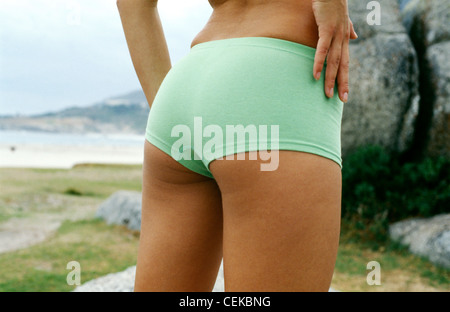 Schuss von weiblichen Bottom in grüne Hotpants, stehend auf einem Strand Meer und Felsen im Hintergrund abgeschnitten Stockfoto