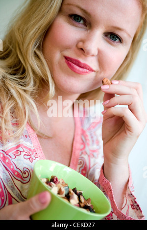 Größere weibliche blonde lange Haare tragen rosa paisley V Neck Shirt hält Schüssel mit gemischten Nüssen und Rosinen in Nahaufnahme Stockfoto