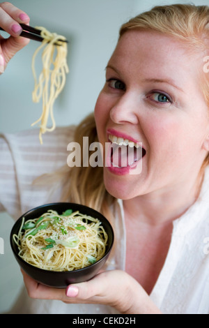 Nahaufnahme eines größeren weibliche blonde Haare im Seite Pferdeschwanz tragen cremefarbene Bluse hält Schüssel Nudeln und Stäbchen anheben, Stockfoto