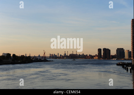 Blauer Himmel Sonnenaufgang anzuzeigen, stromabwärts von der Queensboro Bridge und Manhattan Wolkenkratzer reflektieren, ruhigen Gewässern East River, New York Stockfoto