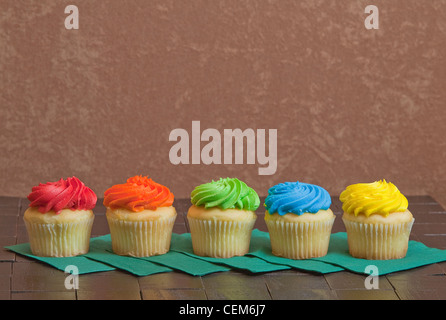 Fünf bunte Cupcakes auf grüne Servietten auf einem Holztisch Stuck im Hintergrund sitzen Stockfoto