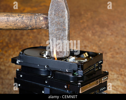 symbolische Daten Zerstörung Thema zeigt die Details eines Hammers auf ein Stapel brennen Festplatten vor rostigen zurück Stockfoto