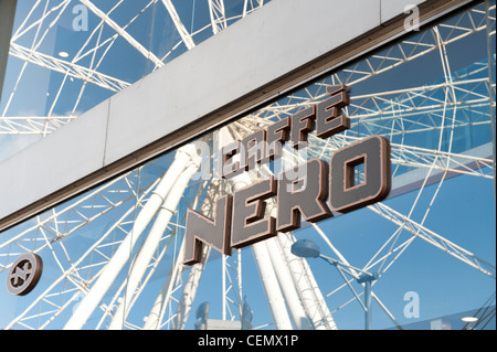 Caffé Nero Coffee Shop-Logo auf Glas-Fenster mit Reflexion der Wheel of Manchester im Hintergrund (nur zur redaktionellen Verwendung). Stockfoto